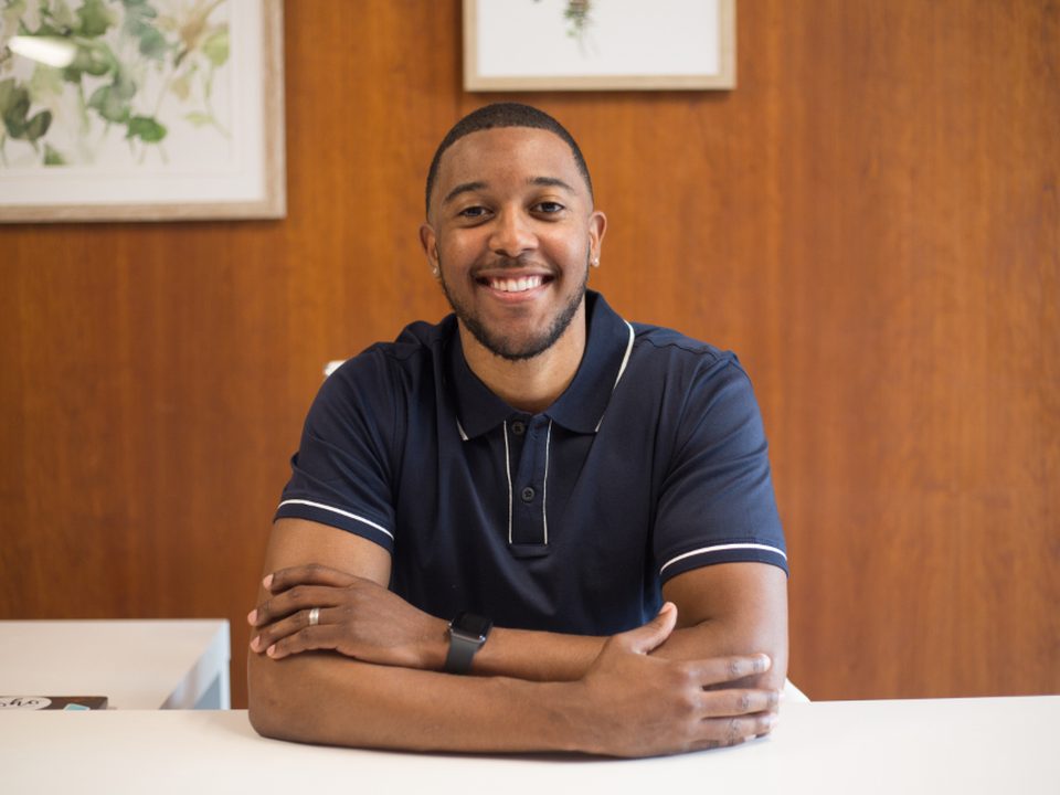A colleague at a desk in an office, smiling toward the camera.